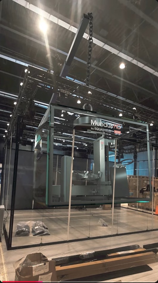Glass-enclosed industrial machine displayed inside a trade show booth during setup